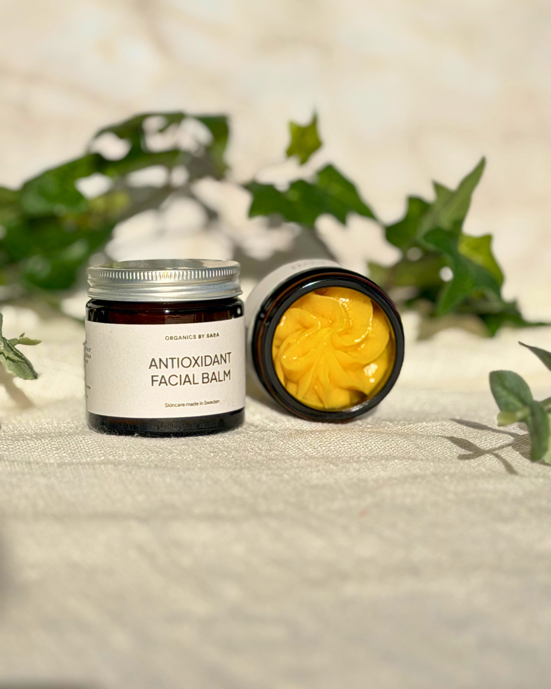 Antioxidant Facial Balm lasipurkissa vihreiden lehtien keskellä
