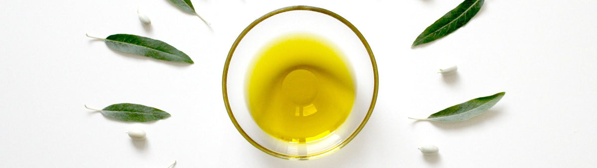 Olivenolie i en glasskål blandt olivenblade