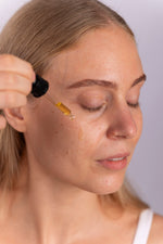 Kvinde drypper Antioxidant Oil Serum på kinden med pipette