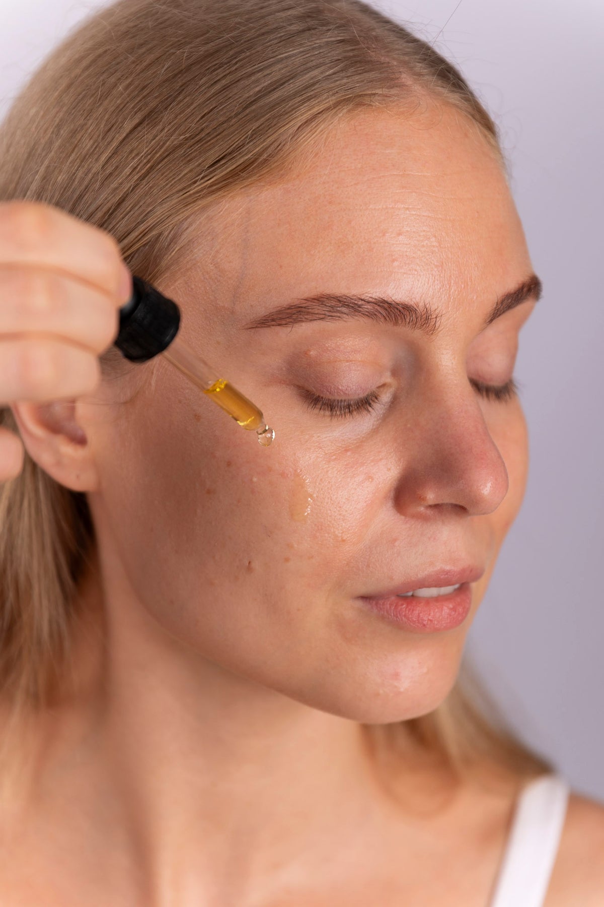 Kvinde drypper Antioxidant Oil Serum på kinden med pipette