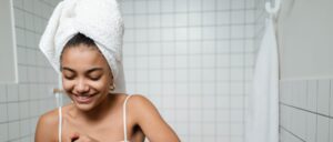 Kvinna med handduk i håret applicerar ekologisk toner på sitt ansikte i ett fräscht badrum.
